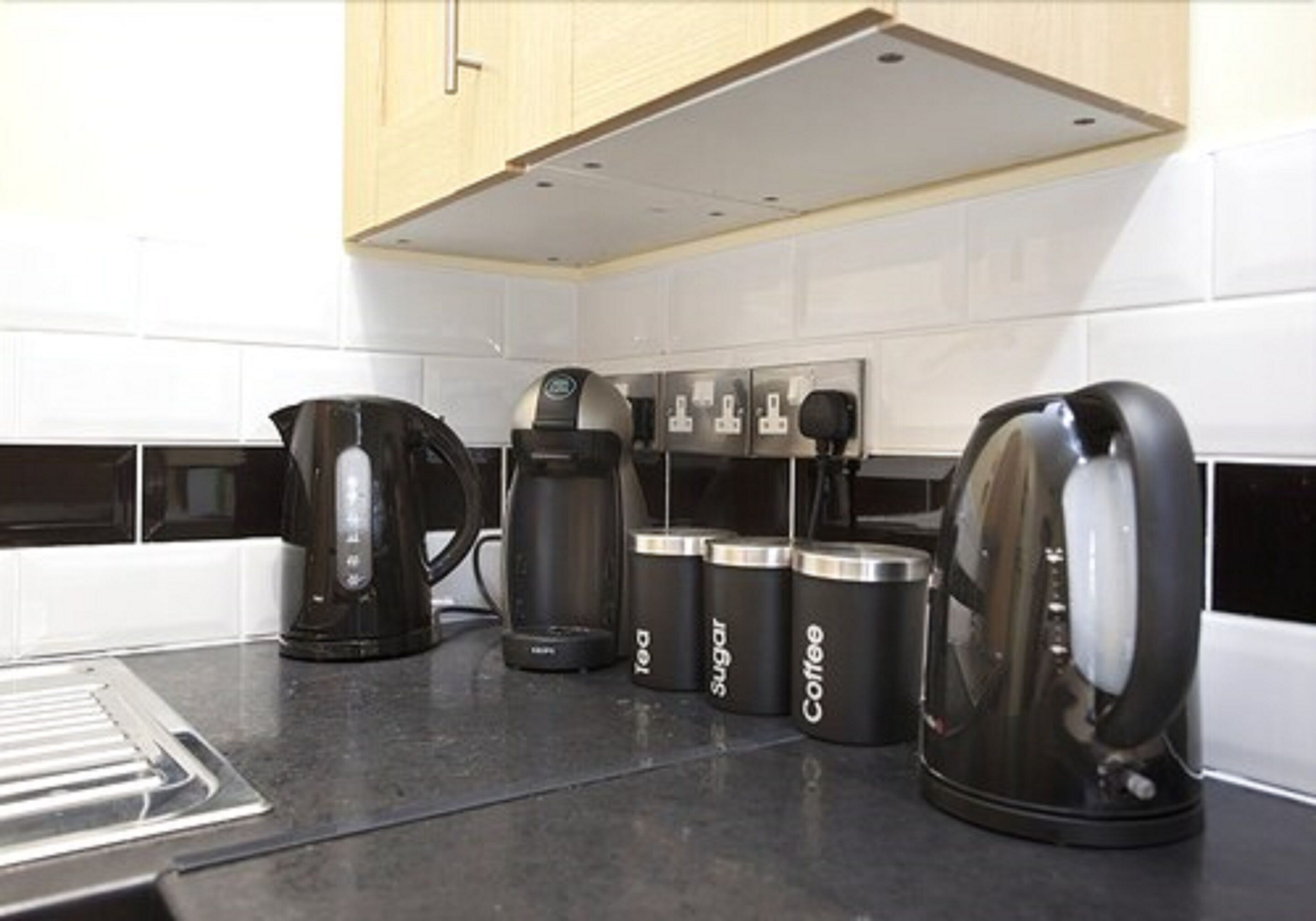 A kitchen with a coffee maker, a kettle, and containers labeled tea, sugar, and coffee.
