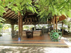Un espacio de estar al aire libre cubierto con una mesa y sillas, una gran rueda decorativa verde y una estructura de madera rústica.