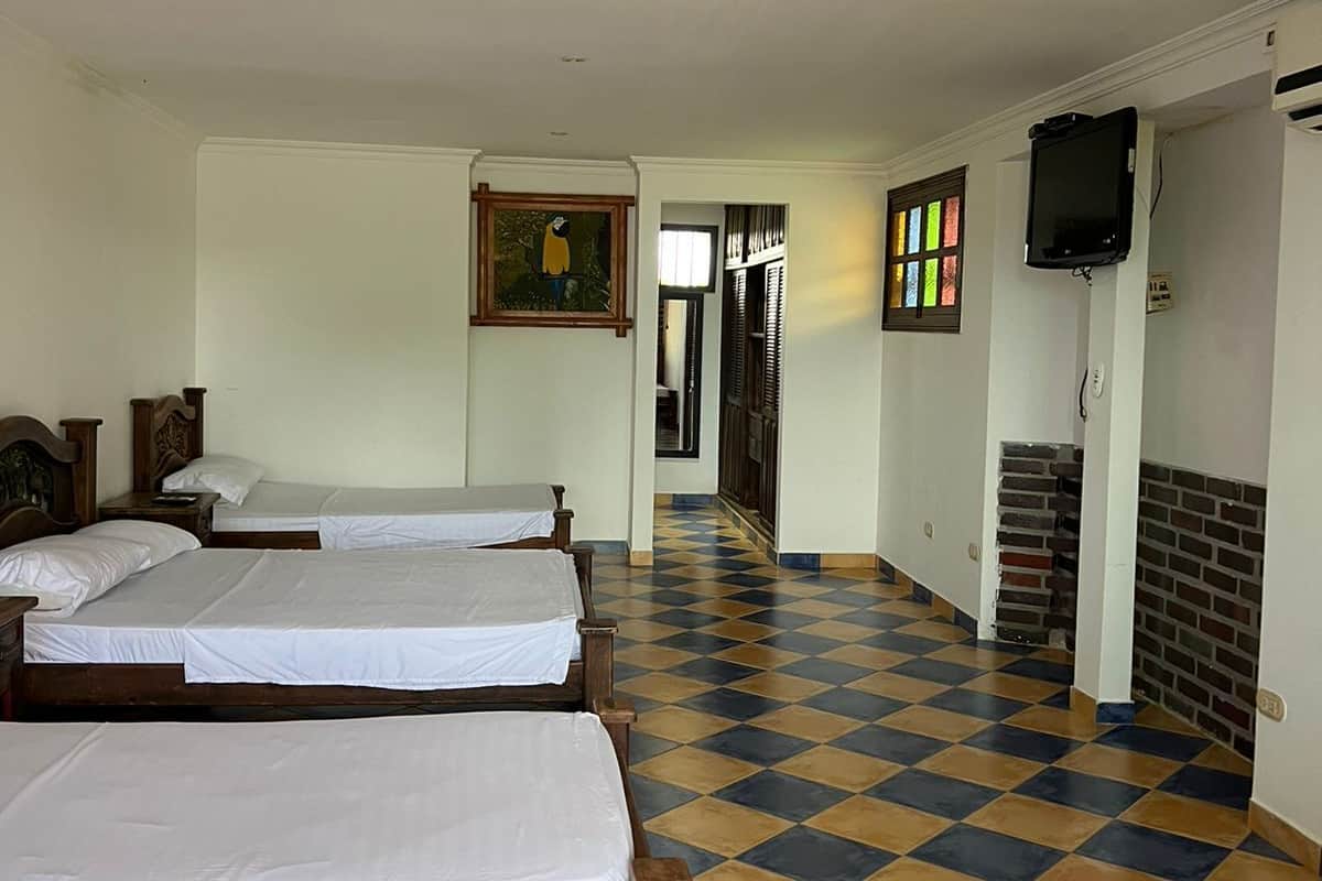 Habitación de hotel con cuatro camas individuales, piso de cuadros, un cuadro en la pared y un televisor montado.