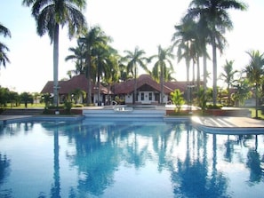 Ein Swimmingpool mit Spiegelung von Palmen, umgeben von einem Gebäude mit rotem Dach und weißen Wänden.