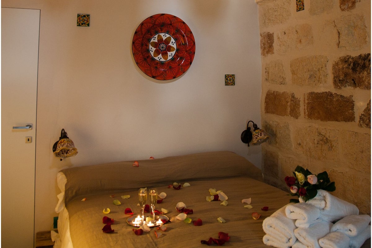 A room with a bed, a decorative plate, and two green bottles on the wall.