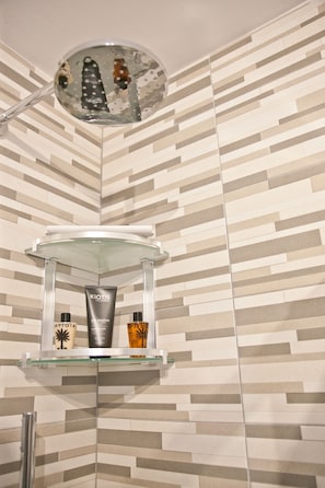 A bathroom with a shower area, a glass shelf with toiletries, and a patterned wall. - B&B Lazzarella (Polignano a Mare)