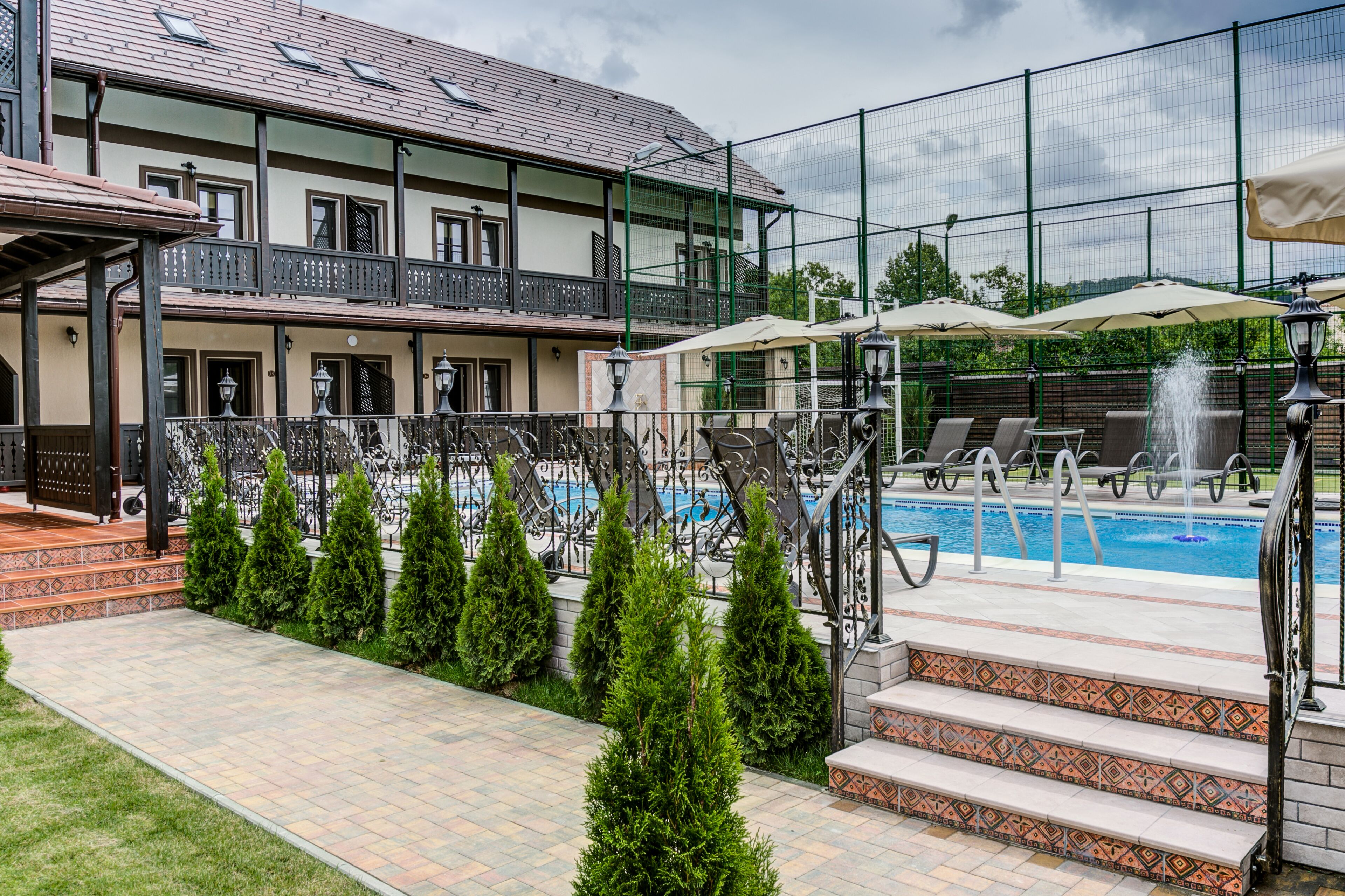 Zona de piscina con un edificio de dos pisos, mobiliario exterior y un patio cercado.