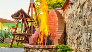 A brick structure with a fire burning inside, surrounded by greenery and a stone wall. - Conacul Ambient (Cristian)