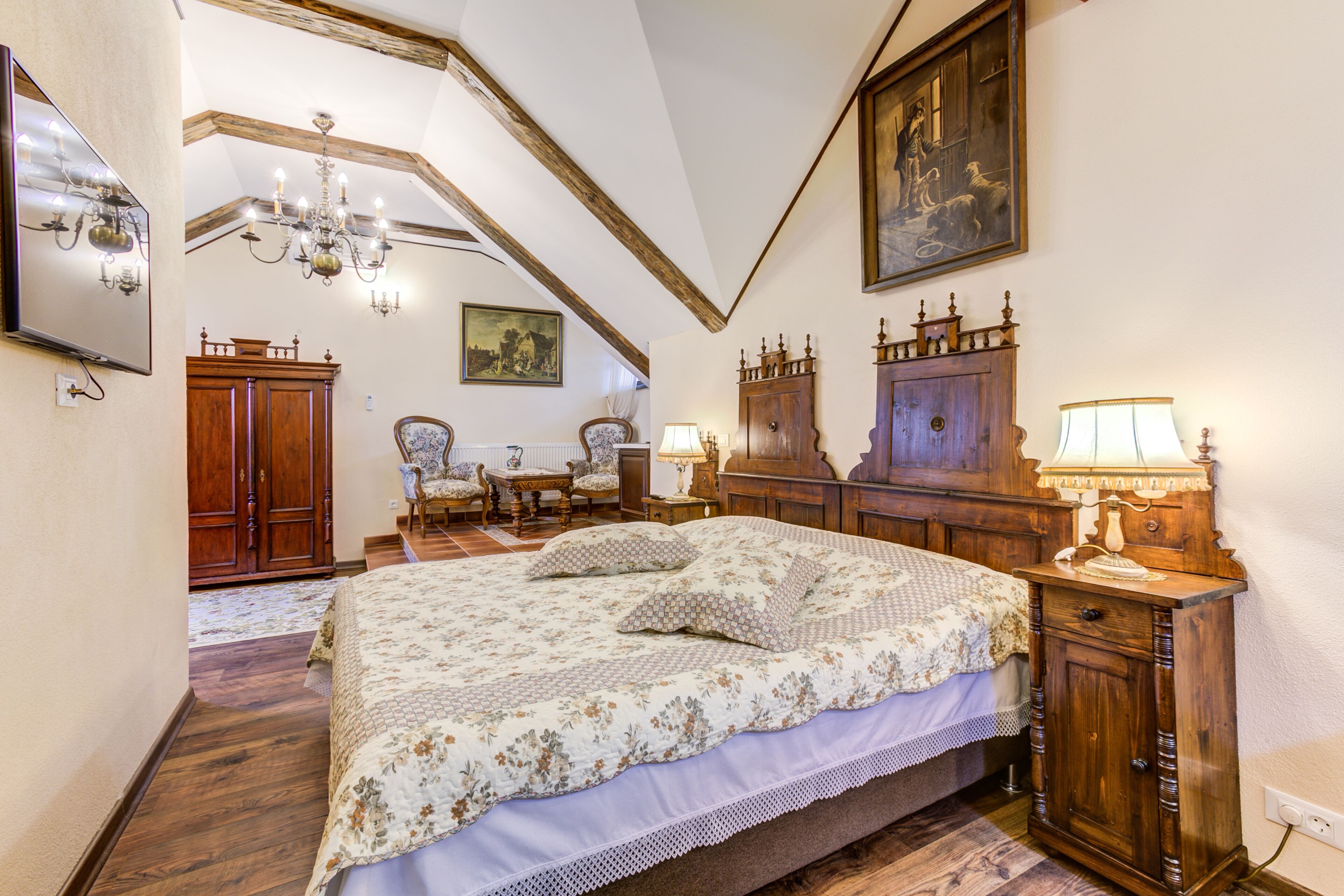 A bedroom with a large bed, wooden furniture, a chandelier, and a painting on the wall.