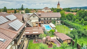A residential area with a swimming pool, tennis court, and a church tower in the background. - Conacul Ambient (Cristian)