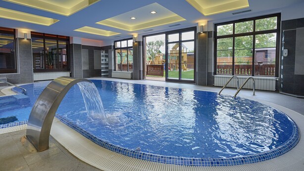 An indoor swimming pool with a clear view of the outside, a modern ceiling design, and a poolside area with a metal structure. - Conacul Ambient (Cristian)
