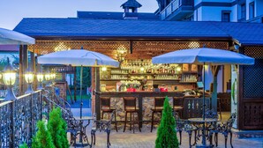 An outdoor bar area with a stone counter, multiple bar stools, and umbrellas providing shade. - Conacul Ambient (Cristian)