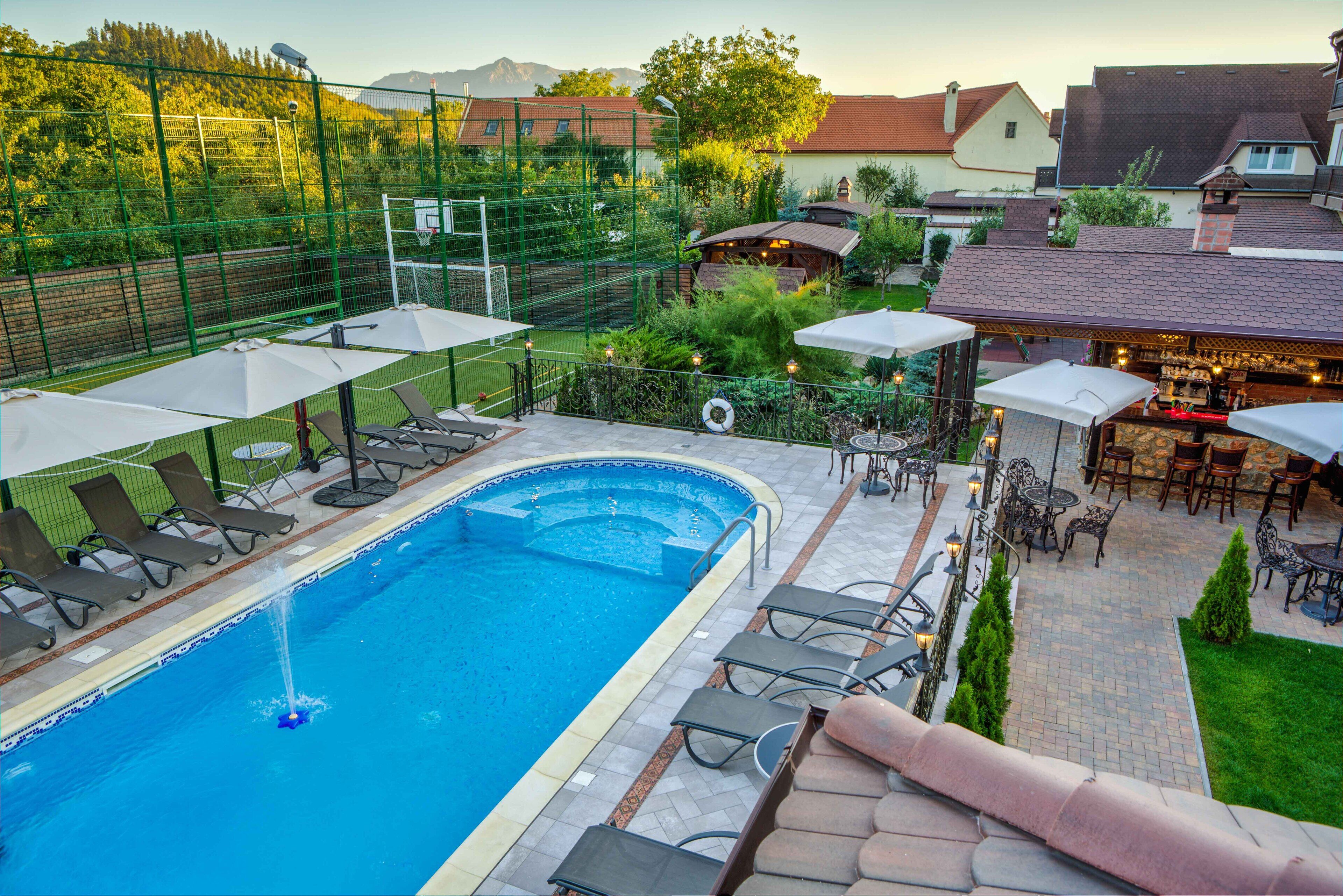A swimming pool with lounge chairs and umbrellas, surrounded by a fenced garden area with a barbecue and outdoor seating.