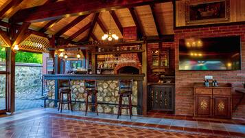 A bar area with a stone counter, wooden stools, a brick fireplace, and a large TV screen.