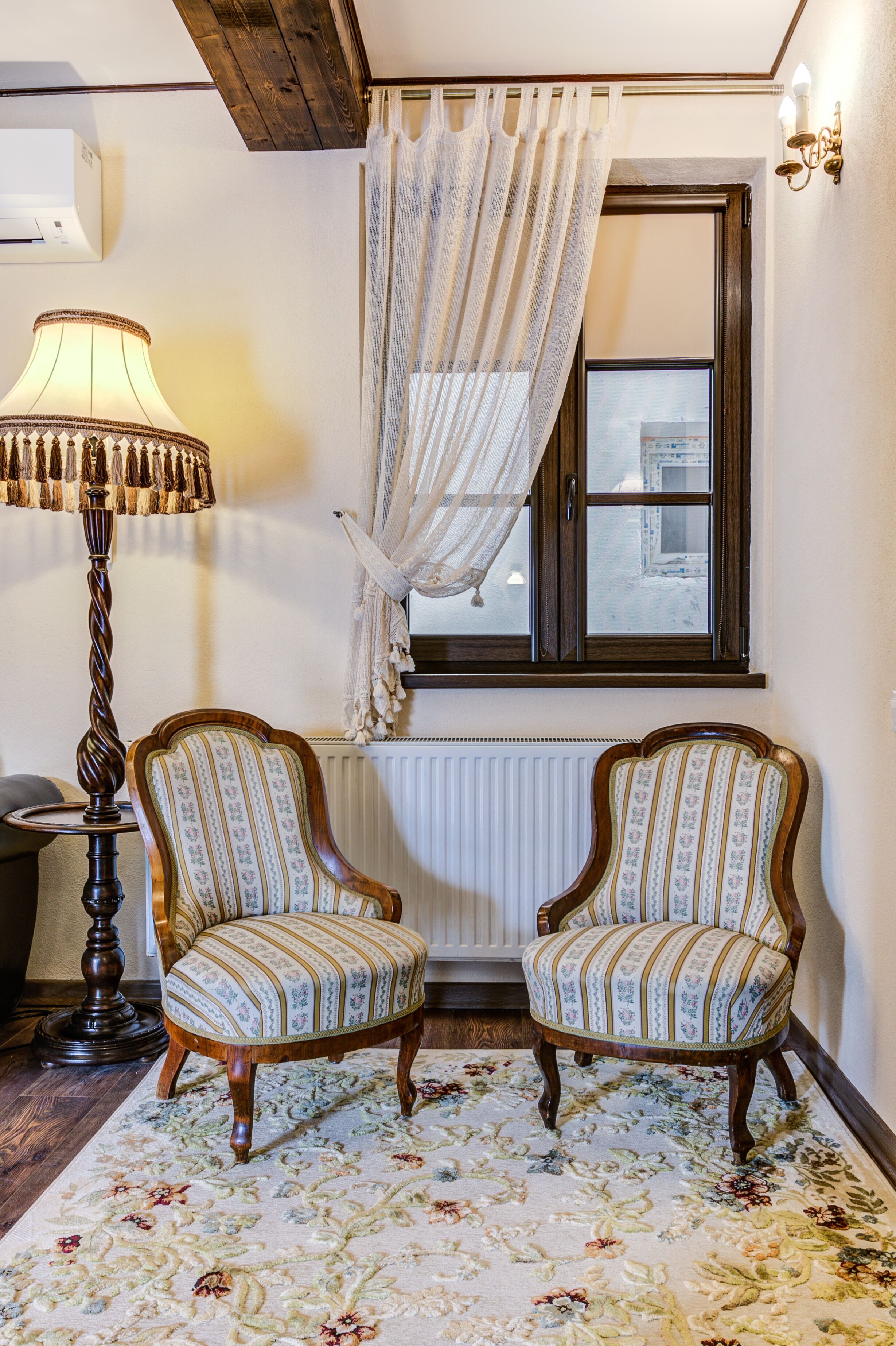Une pièce comprenant deux fauteuils rembourrés, une lampe sur pied, une fenêtre avec un rideau et un radiateur.