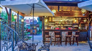 An outdoor bar area with a stone wall, wooden bar counter, and metal chairs. - Conacul Ambient (Cristian)