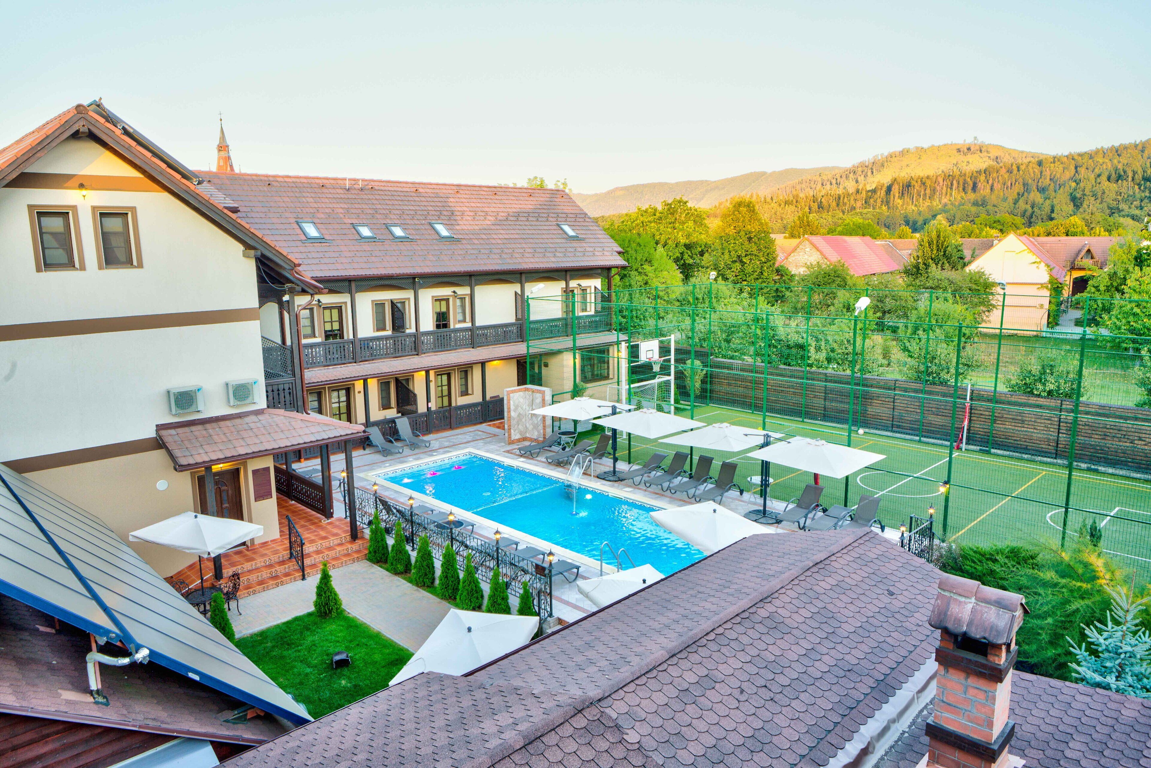 En boligbygning med swimmingpool, udendørs møbler og tennisbane.