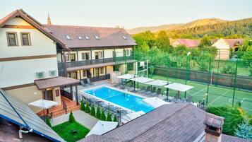 En boligbygning med swimmingpool, udendørs møbler og tennisbane.
