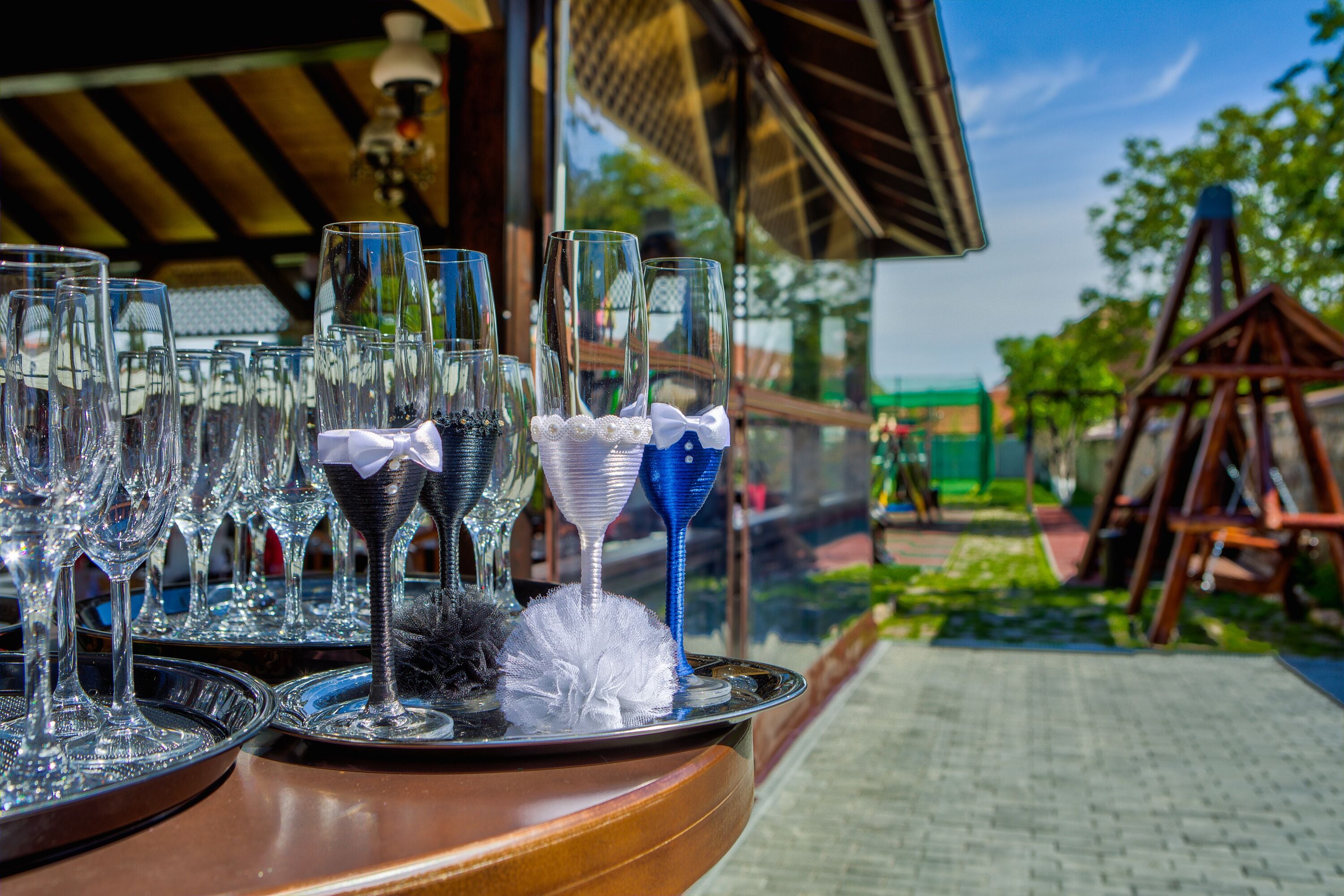 A table with multiple wine glasses and a decorative bowl, set outdoors with a wooden structure and greenery in the background.
