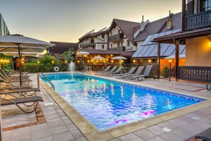 Piscina com espreguiçadeiras e guarda-sóis, cercada por edifícios com varandas e áreas de estar ao ar livre.