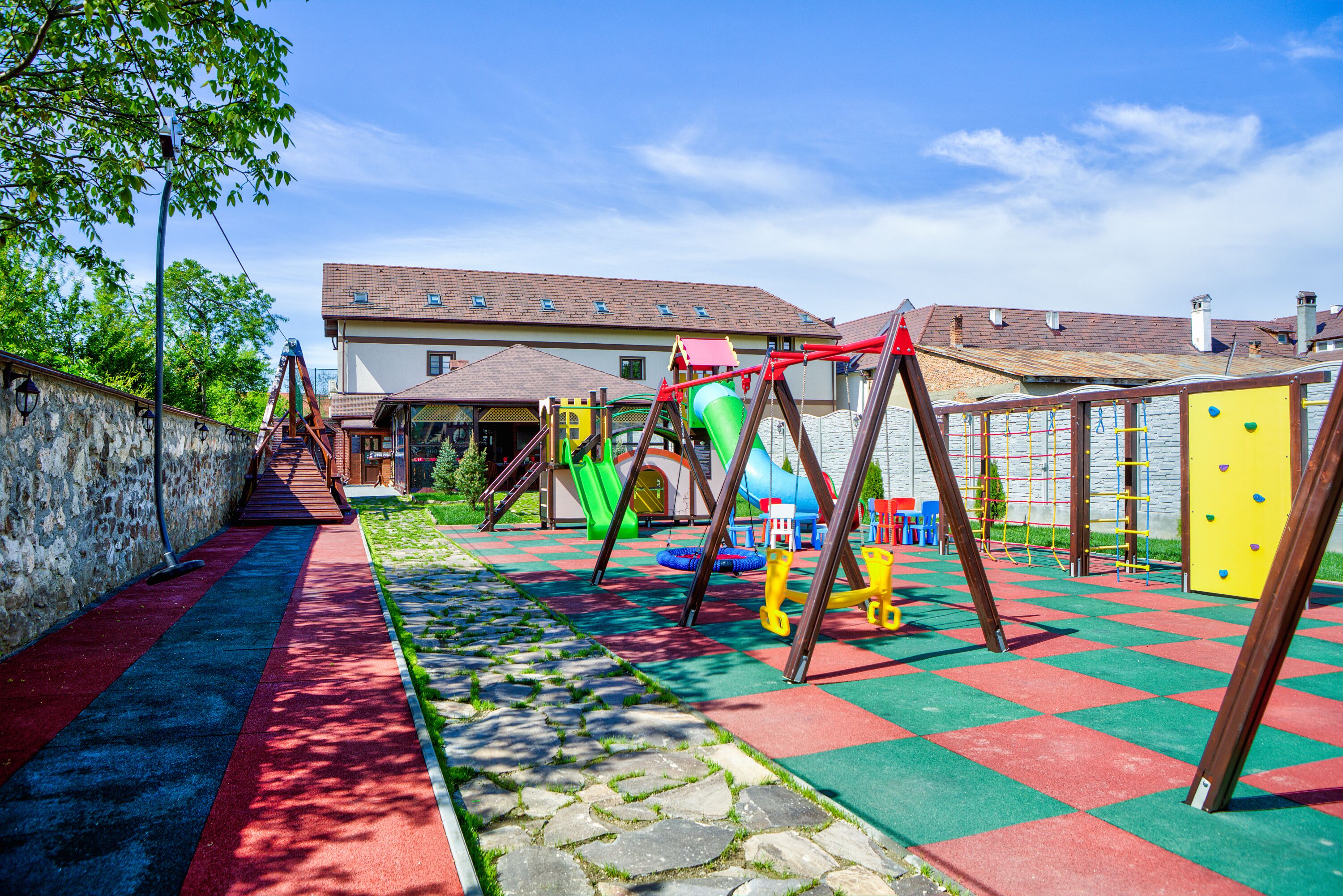 Un parque infantil con diverso equipo de juegos, un camino de piedra y un edificio al fondo.