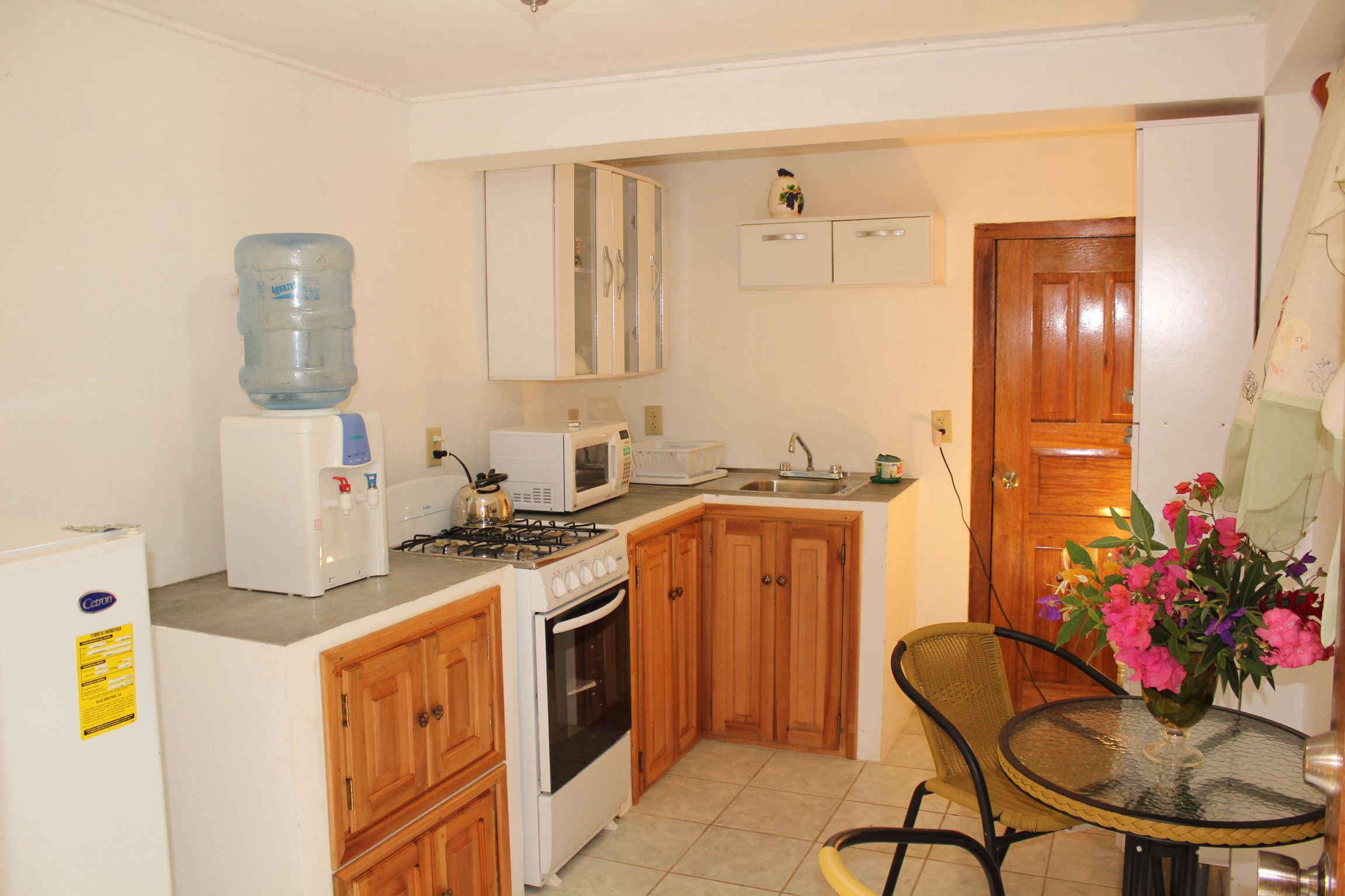 Una cocina compacta con refrigerador, microondas, estufa, horno y dispensador de agua.