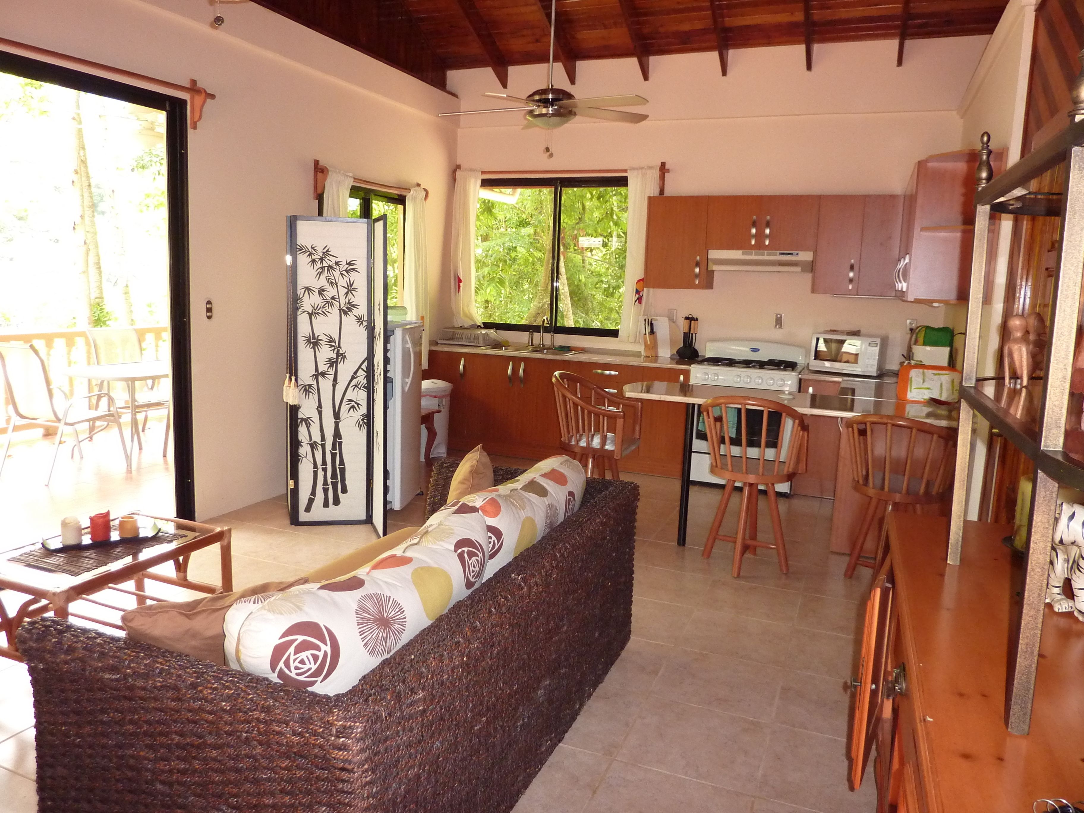 A compact kitchen with a stove, microwave, and cabinets. There is a dining area with a table and chairs, and a sofa with patterned cushions.