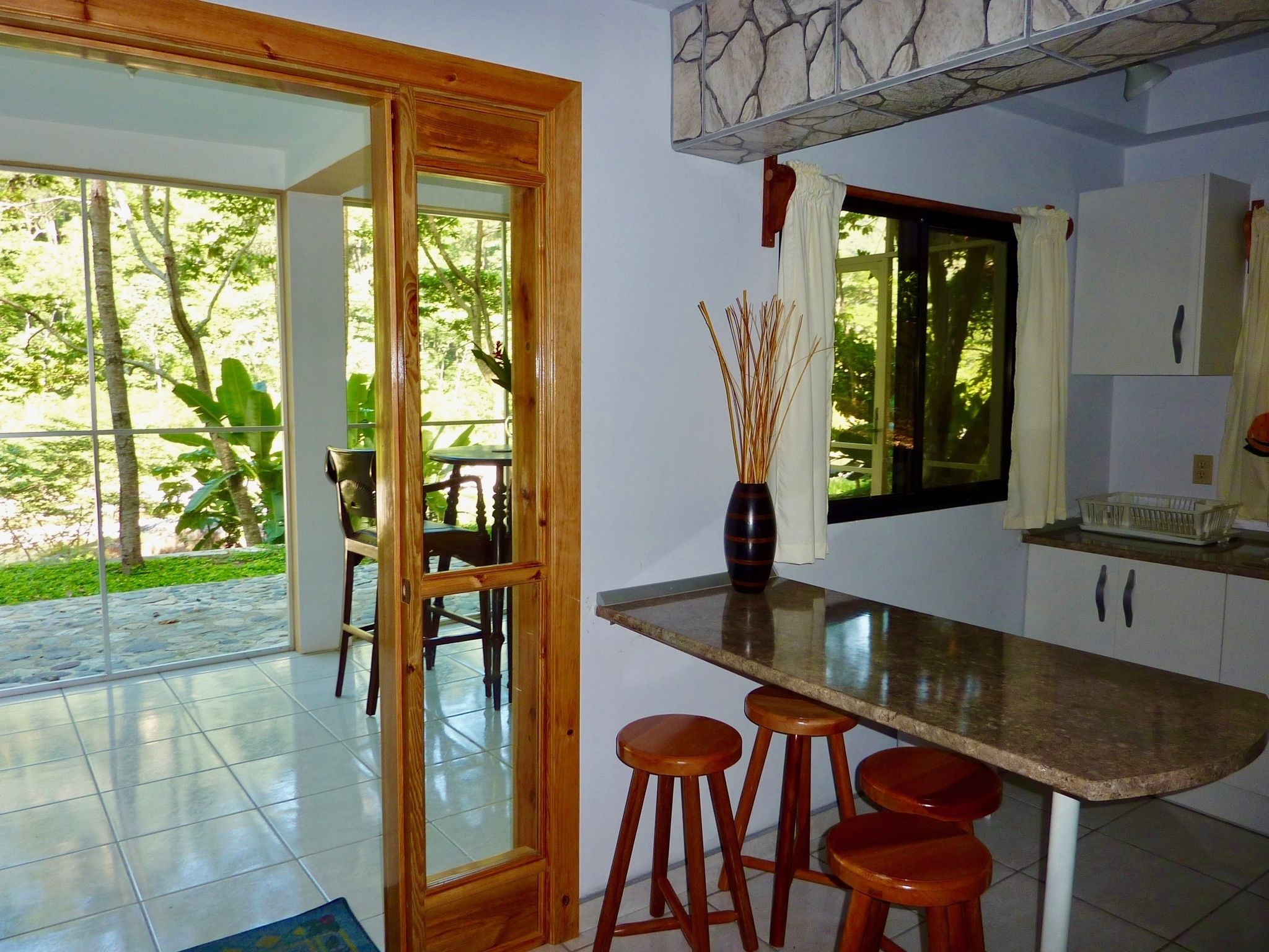 A kitchen with a wooden door leading to a patio area, a vase with reeds, and a window with curtains.