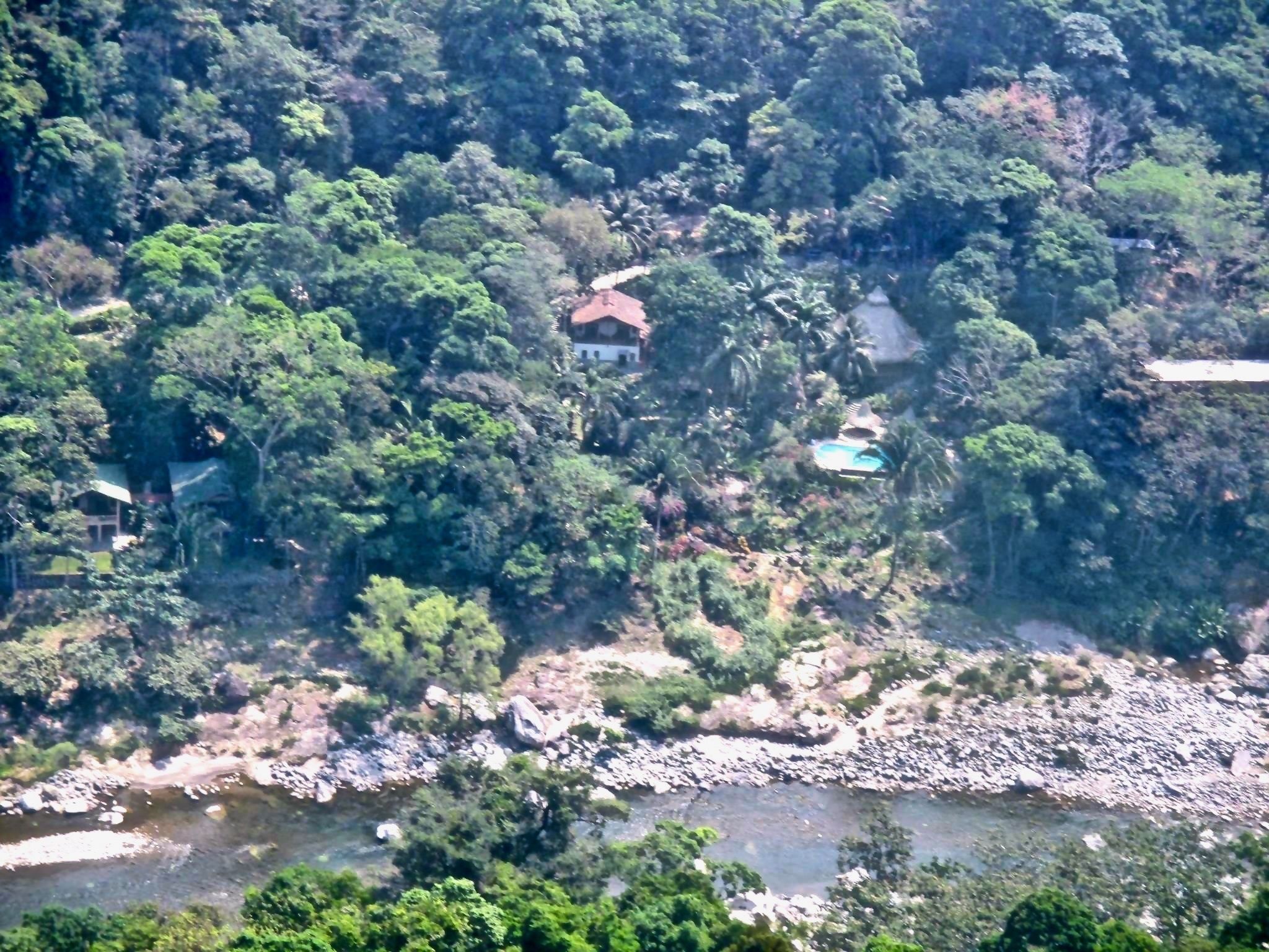 Una casa envoltada de bosc dens, un riu al primer pla i una petita piscina.