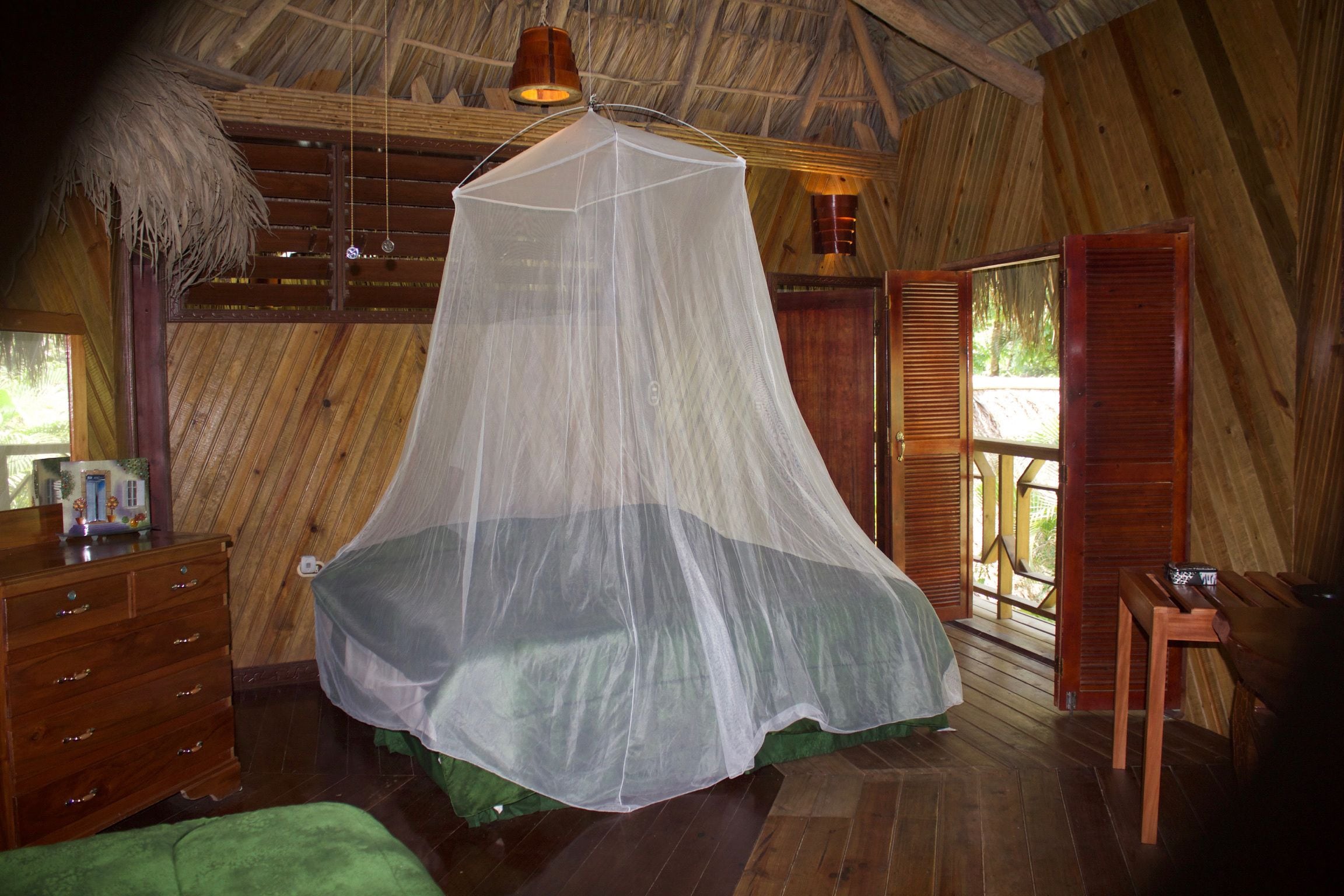 Una habitación con una cama bajo una mosquitera, paredes de madera, un aparador y un banco.