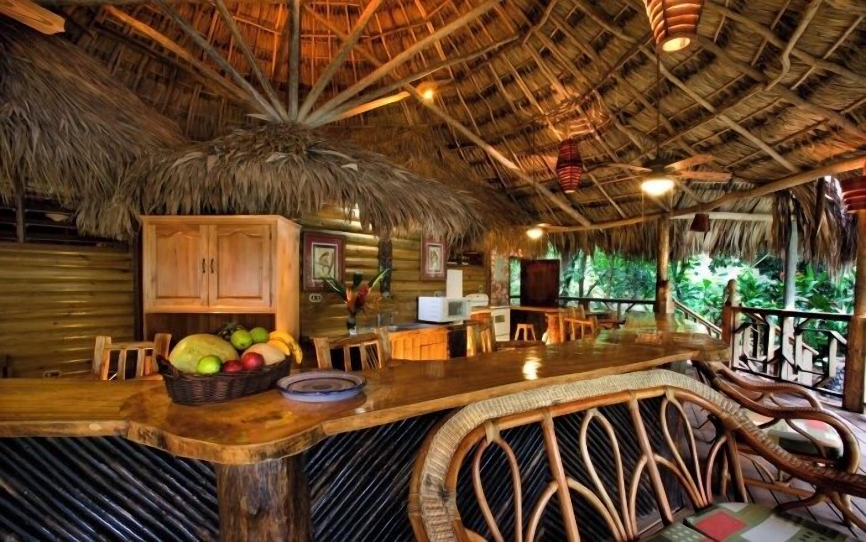 Interior rústico de madera con techo de paja, una zona de bar con mobiliario de mimbre y vistas al exterior.
