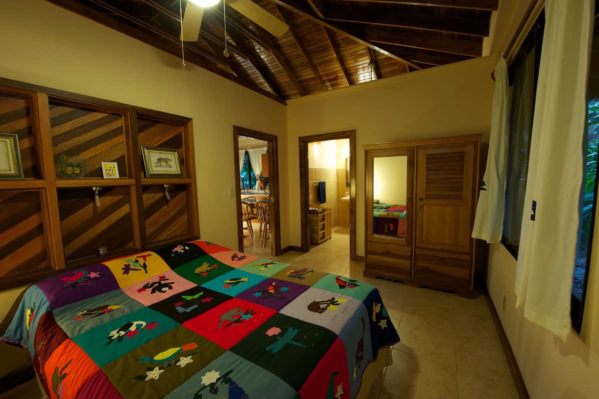 Quarto com um edredom colorido, prateleiras de madeira e teto com vigas aparentes.