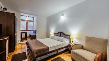 A bedroom with a bed, bedside table, chair, wardrobe, and a window with blinds.