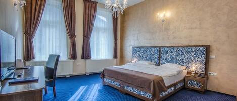 A hotel room with a large bed, a desk, a chair, a chandelier, and a patterned headboard.