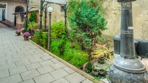 A paved courtyard with a metal grill, a small tree, and potted plants. - Residence Central Annapolis (Brasov)