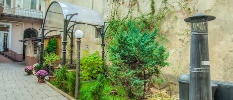 A paved courtyard with a metal grill, a small tree, and potted plants.