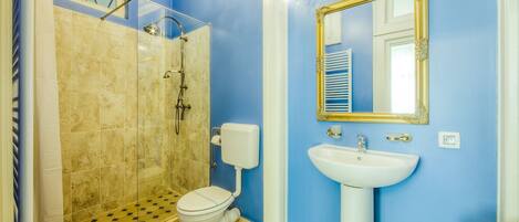 A bathroom with a shower, toilet, sink, and a mirror with a gold frame.