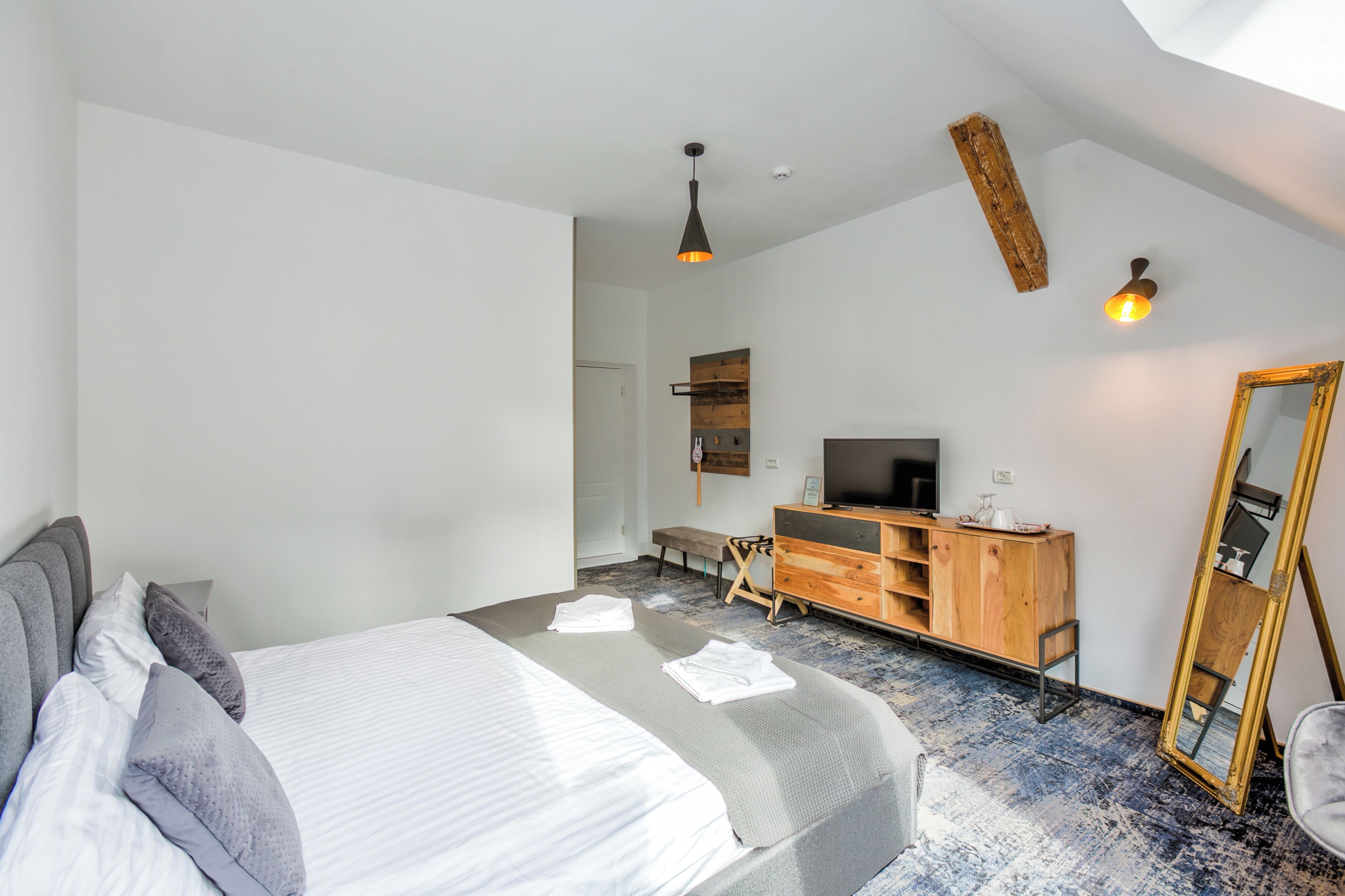 Une chambre moderne avec un grand lit, une commode en bois, une télévision et un miroir.