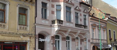 A multi-story building with a pink facade, a visible storefront with a sign, and a street in front.