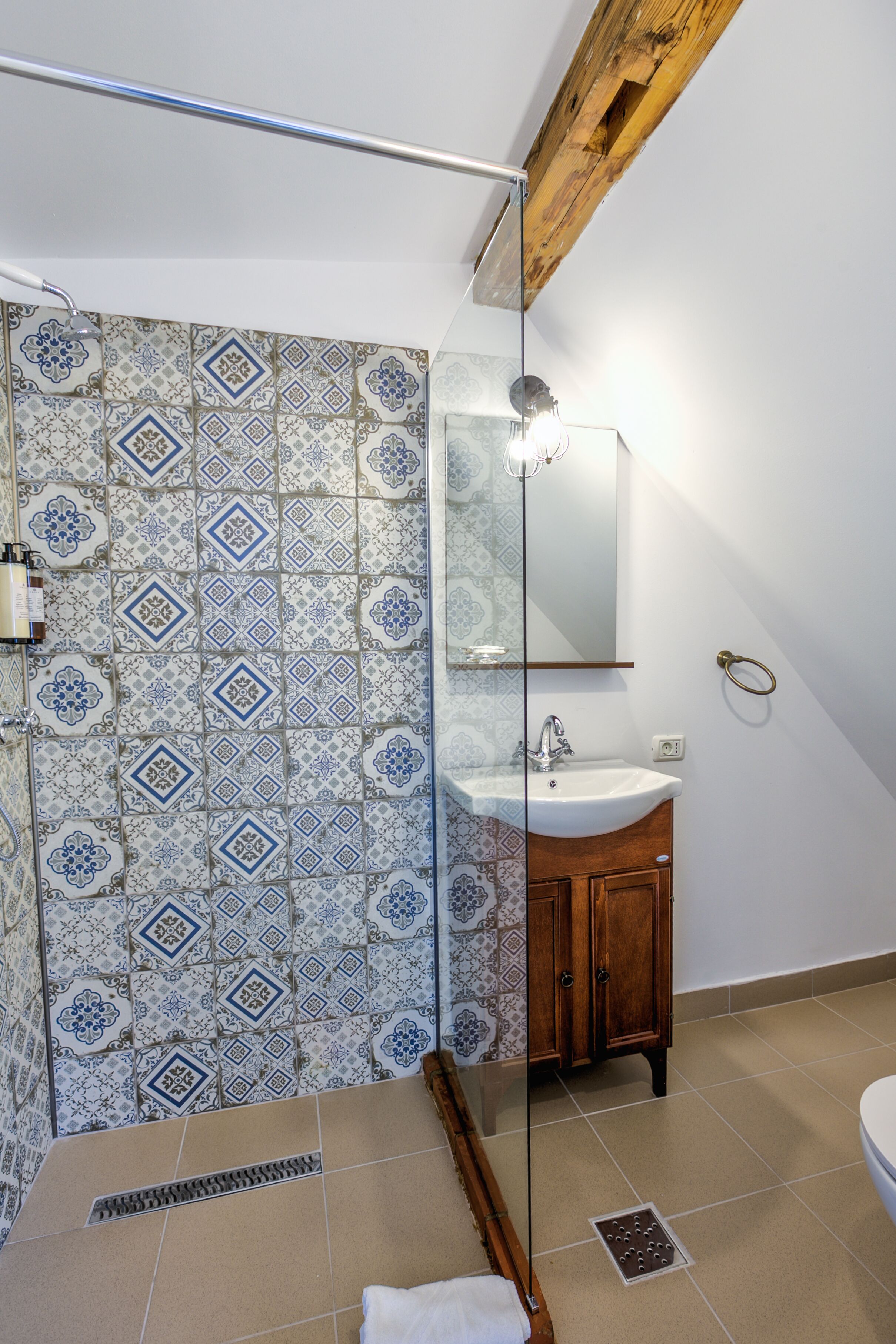 A bathroom with patterned tiles, a wooden cabinet, a sink, and a glass shower enclosure.