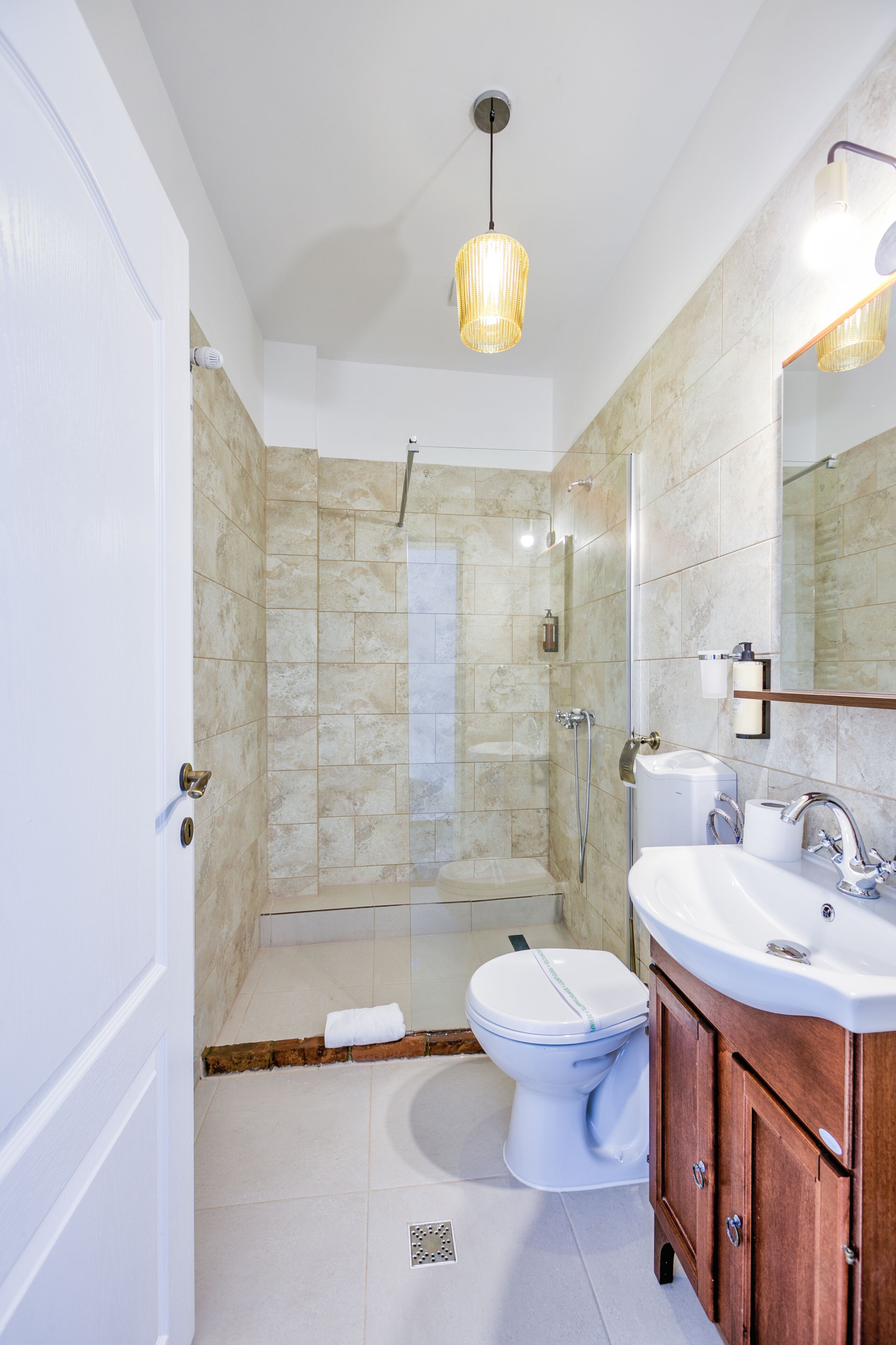 Une salle de bain moderne avec une douche à parois de verre, des toilettes blanches, un lavabo avec un miroir et un meuble-lavabo en bois.
