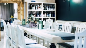 A dining area with white chairs, a long table, and a wine rack in the background. - Residence Central Annapolis (Brasov)