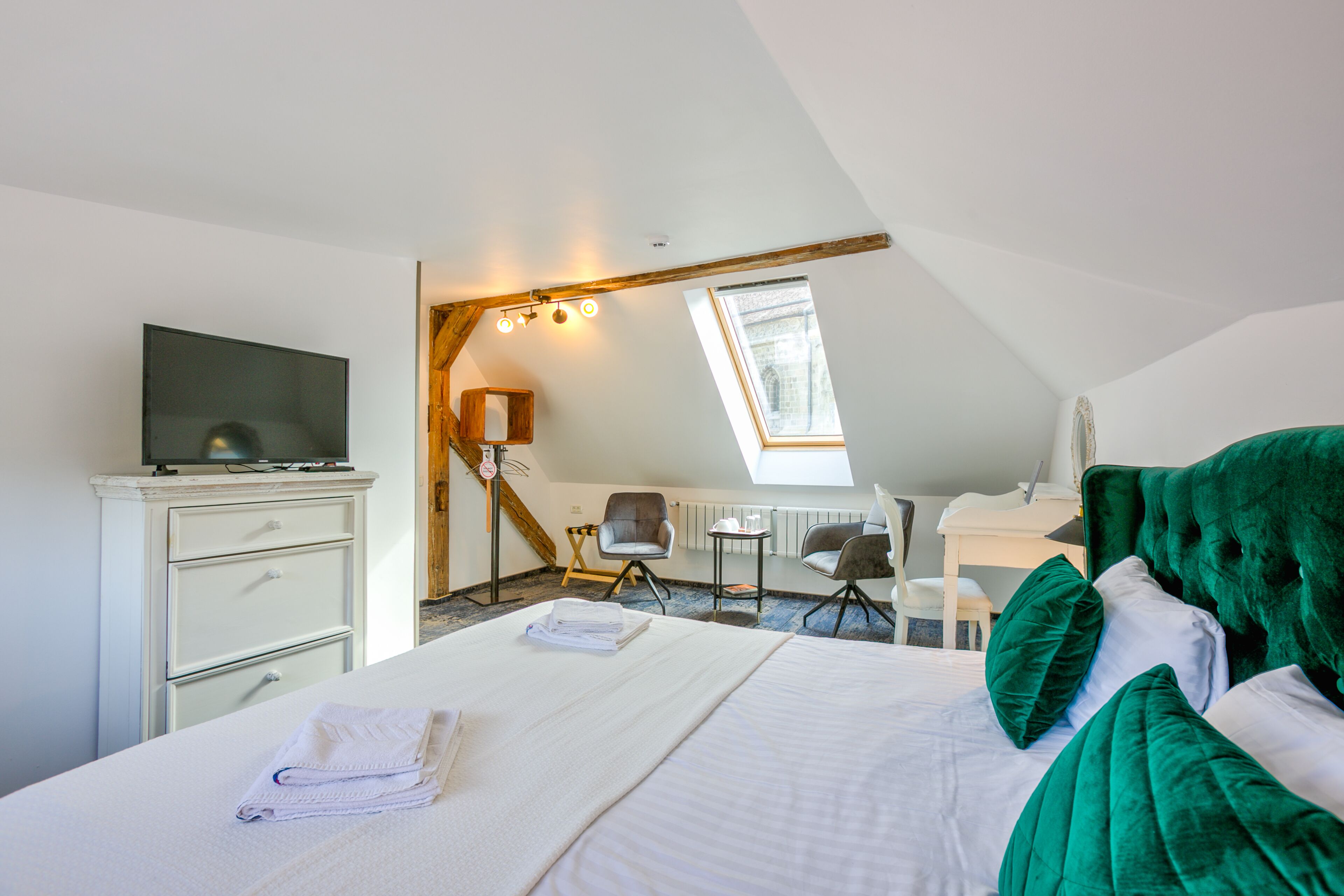 Habitación de hotel con cama, escritorio, silla, televisor y tragaluz.
