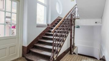 Una escalera con barandilla de madera y alfombra estampada, que conduce a un rellano con una puerta y ventanas.