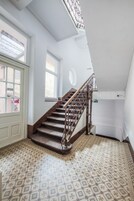 Una escalera con barandilla de madera y alfombra estampada, que conduce a un rellano con una puerta y ventanas.