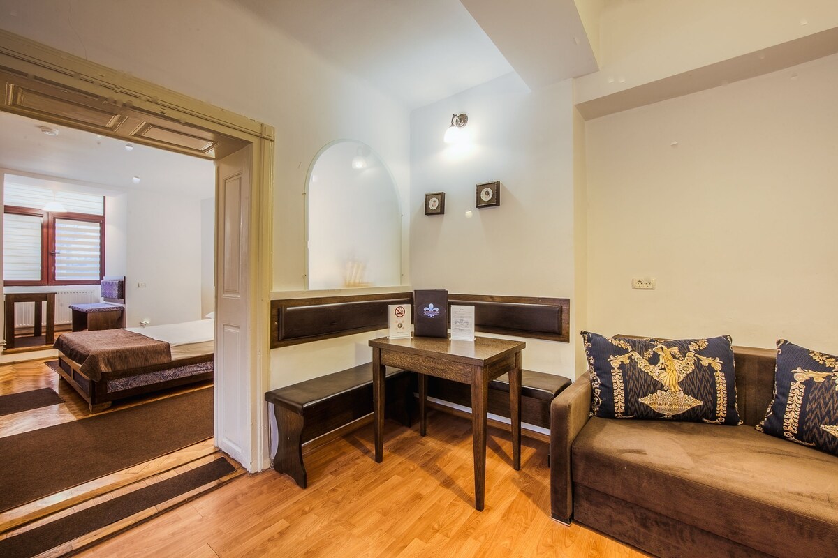 A room with a wooden bench, a small table, a sofa with decorative pillows, and a doorway leading to another room.