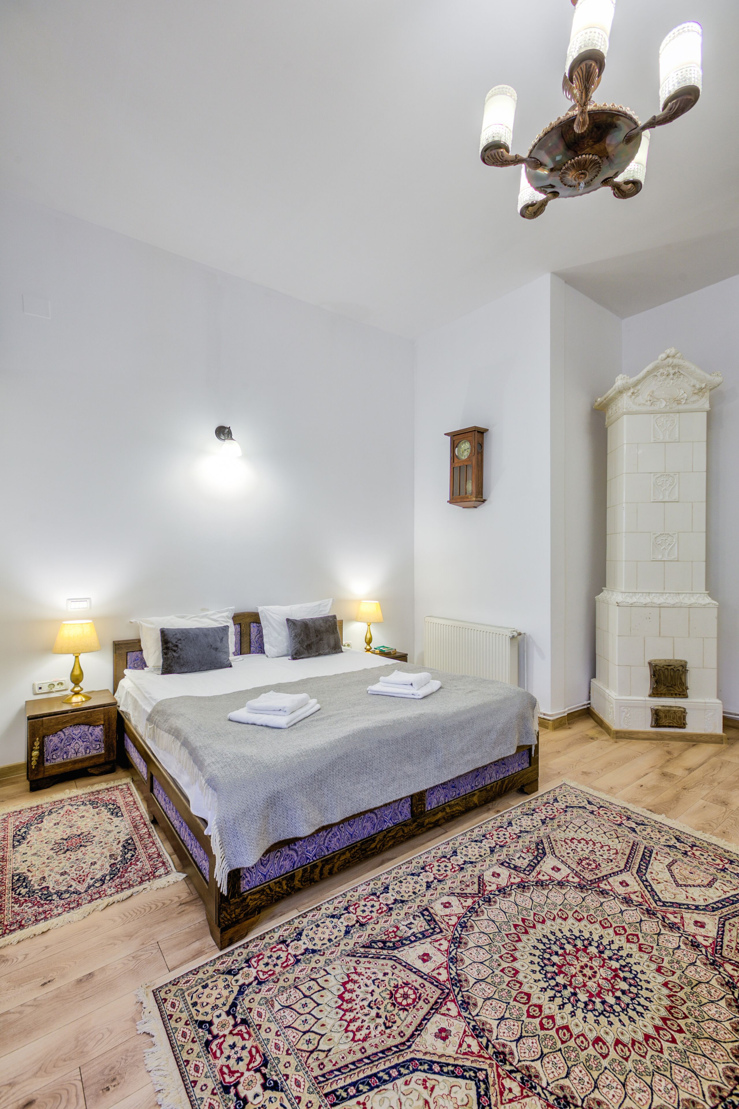 Un dormitorio con una cama, dos lámparas de noche, un candelabro, un reloj, una chimenea y dos alfombras.