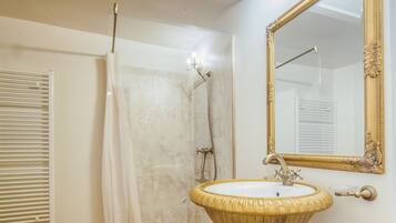 A bathroom with a pedestal sink, a large mirror, and a shower area.