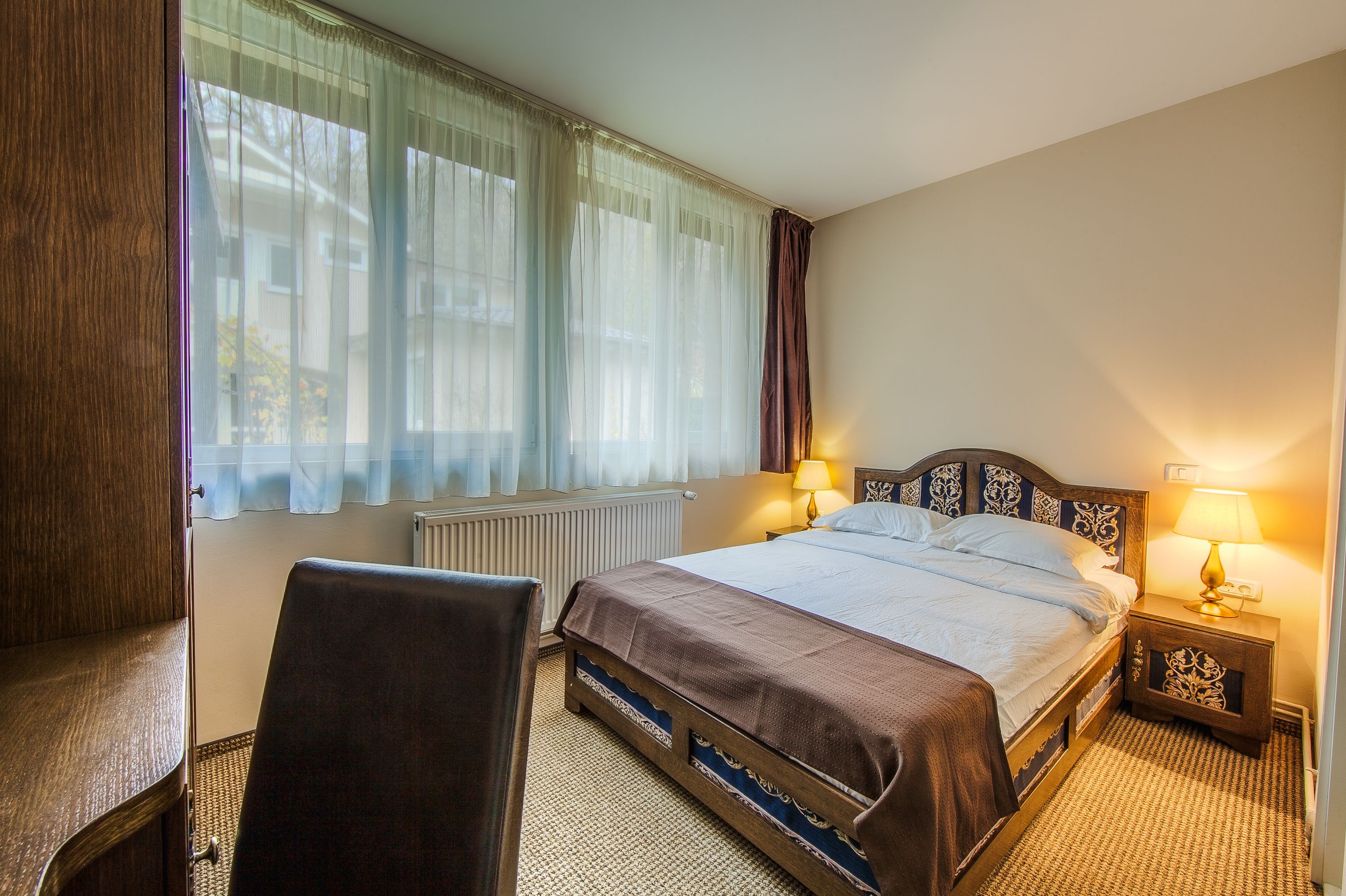 A hotel room with a bed, bedside table, lamp, chair, and a window with curtains.