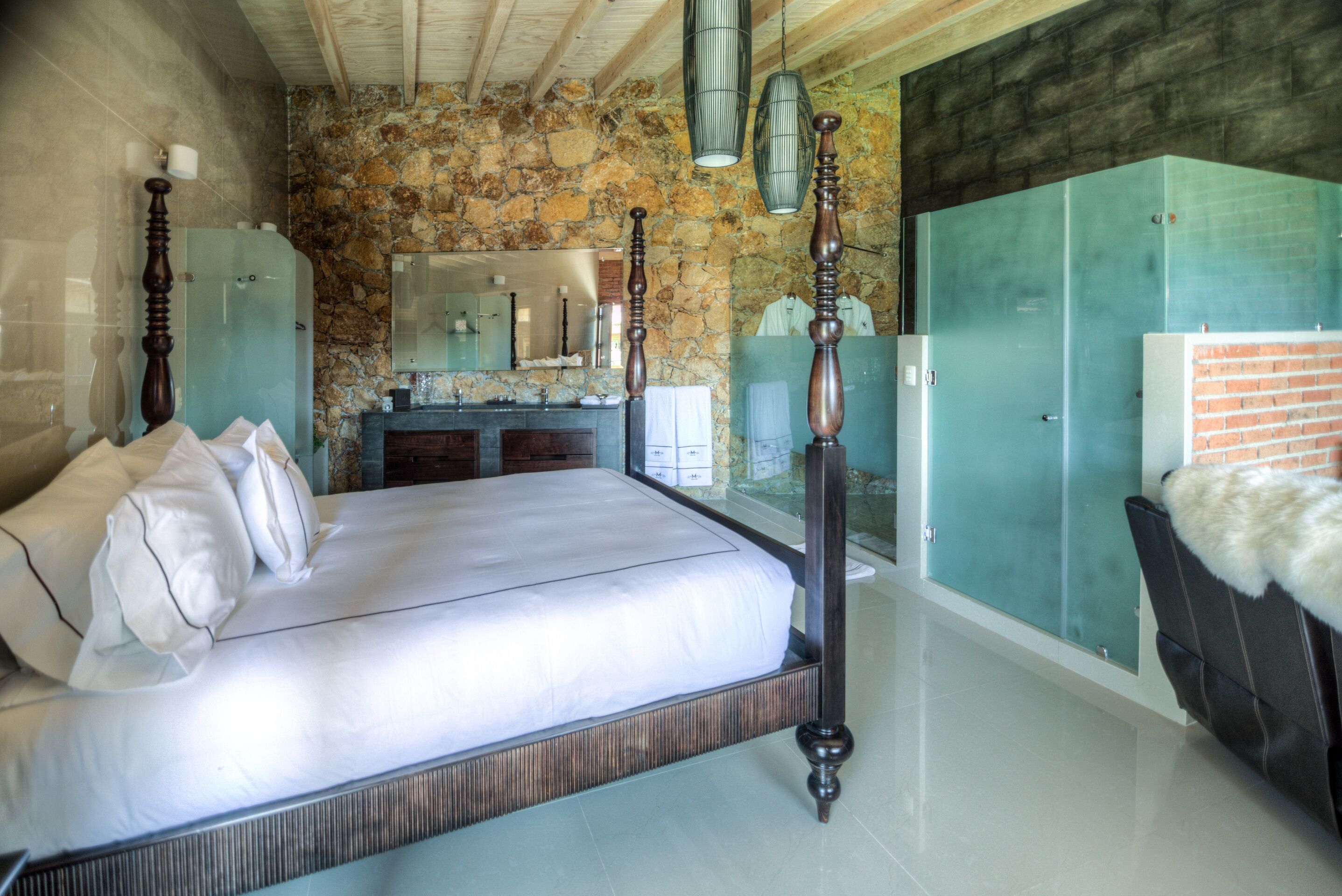 A bedroom with a stone wall, a wooden bed, a vanity with a mirror, and a wardrobe.