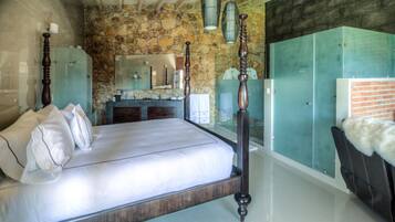 A bedroom with a stone wall, a wooden bed, a vanity with a mirror, and a wardrobe.