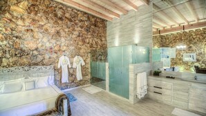 Uma casa de banho moderna com parede de pedra, chuveiro com divisória de vidro, banco de madeira e um espelho grande.
