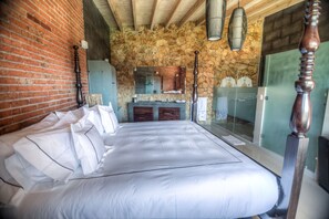 A bedroom with a large bed, a stone wall, a brick wall, and a wooden ceiling.