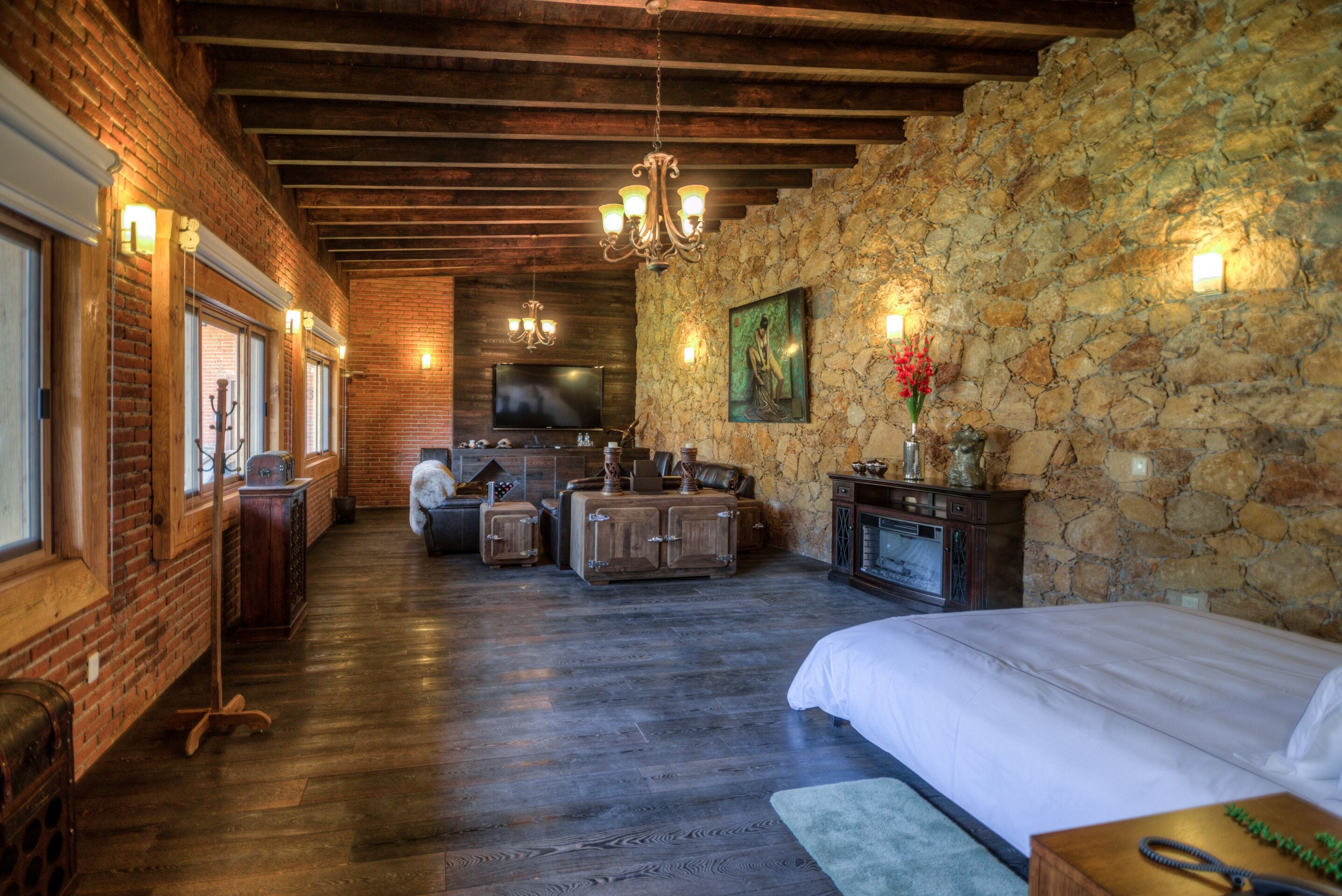 Una habitación de hotel rústica con pared de piedra, piso de madera, una cama grande, un televisor y chimenea.
